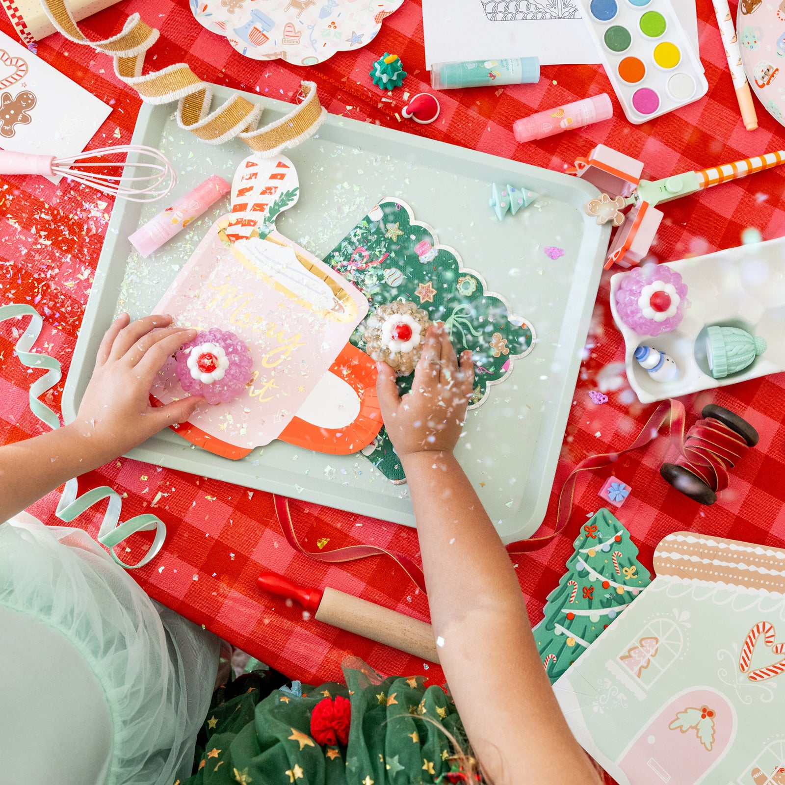 Children's hands playing with Christmas-themed toys on a red tablecloth.
